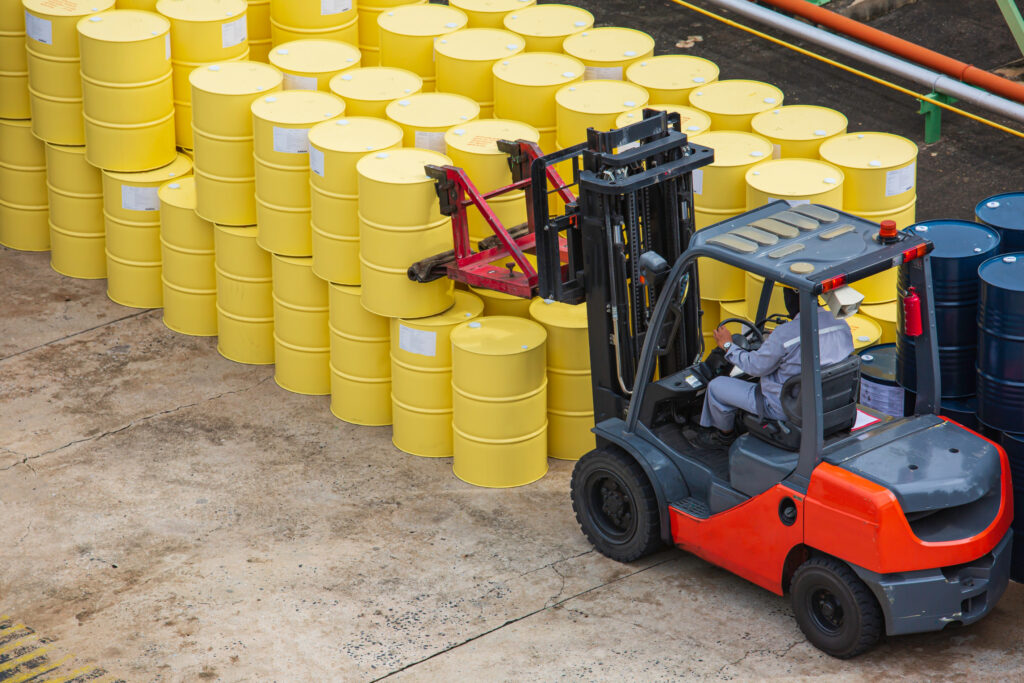 An orange diesel counterbalance forklift moving yellow barrels. 