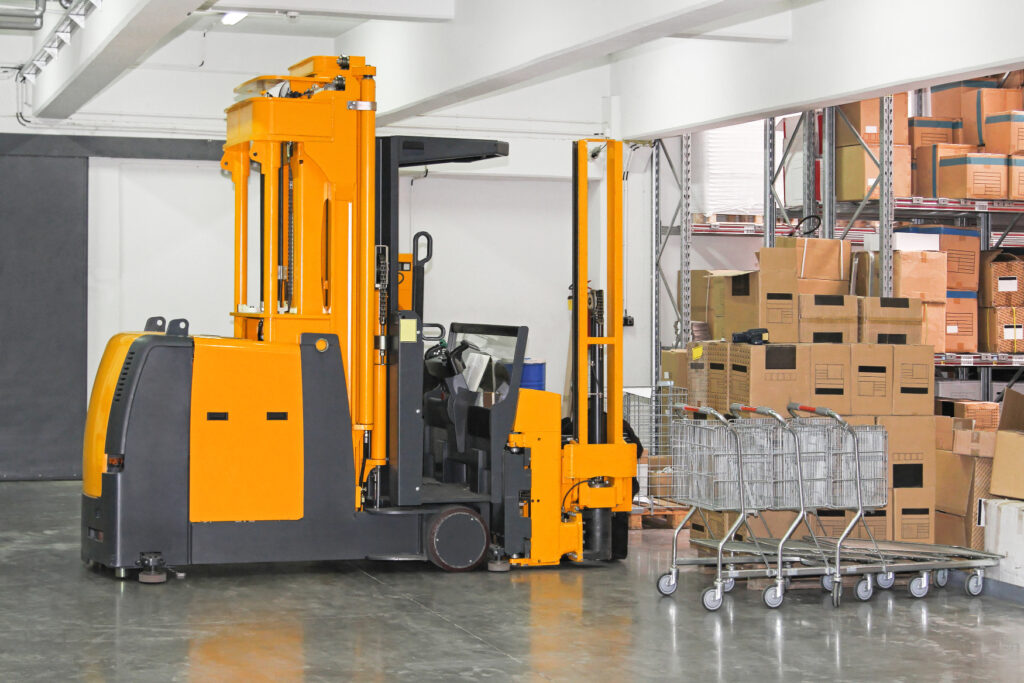 A yellow VNA (very narrow aisle) rail guided forklift, moving a pallet. 